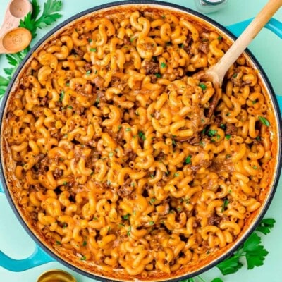 skillet of homemade hamburger helper garnished with chopped fresh parsley. background is light aqua colored.