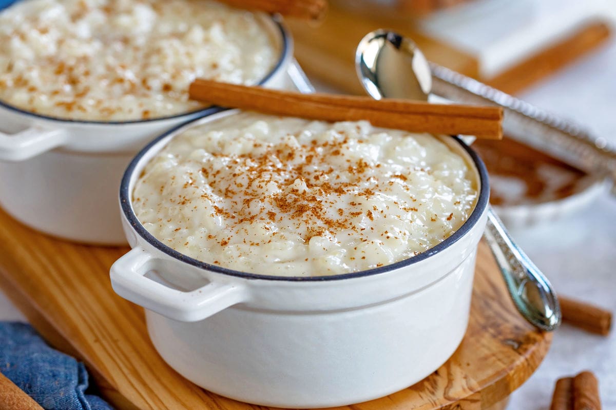 rice pudding served in 2 small white cast iron pots with cinnamon sticks resting on the rim.