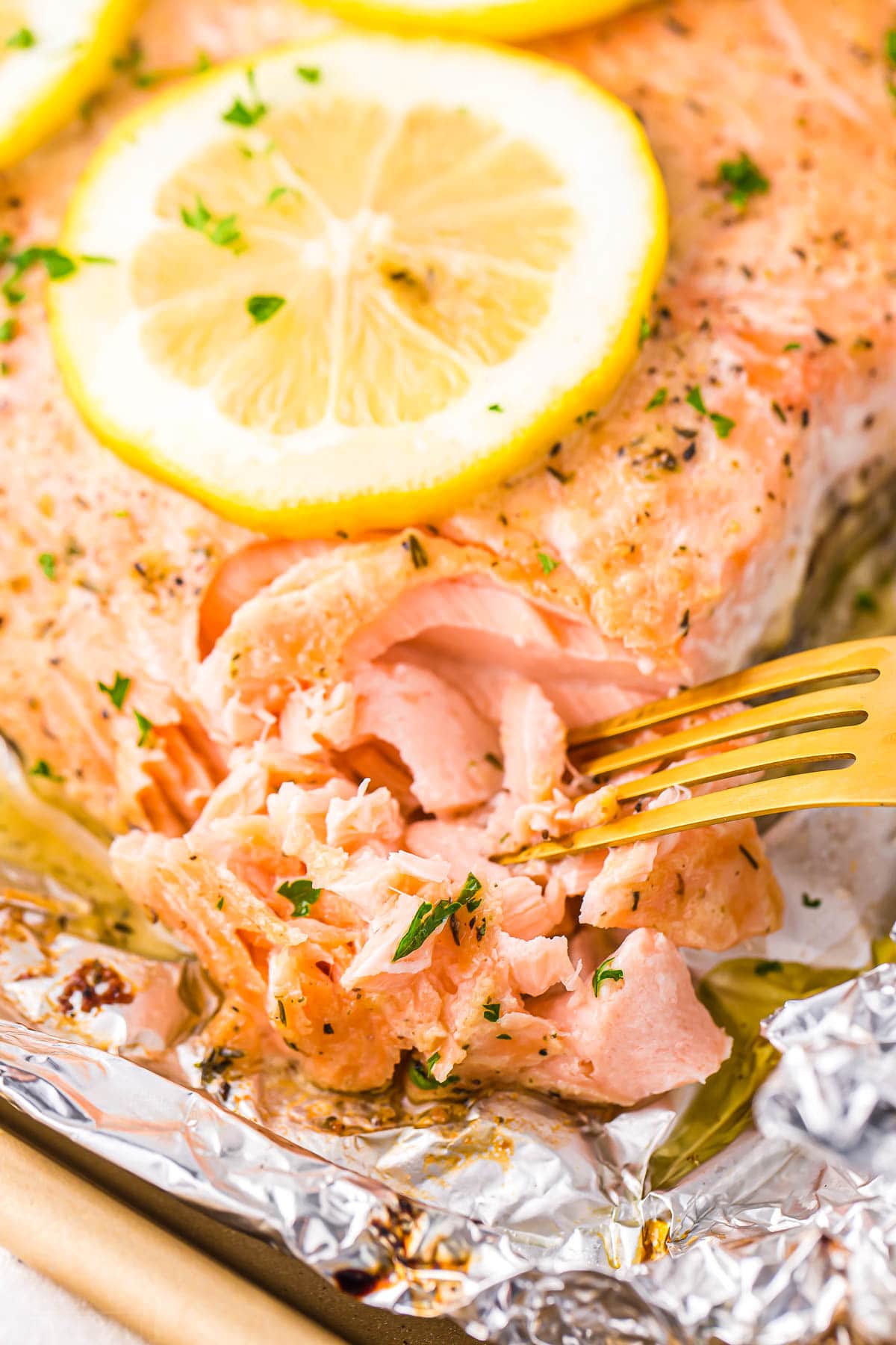 tender flaky salmon being flaked with a gold fork on a large salmon filet topped with a lemon slice.