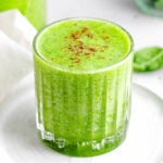 simple green smoothie recipe in glass sitting on small white plate in front of blender.