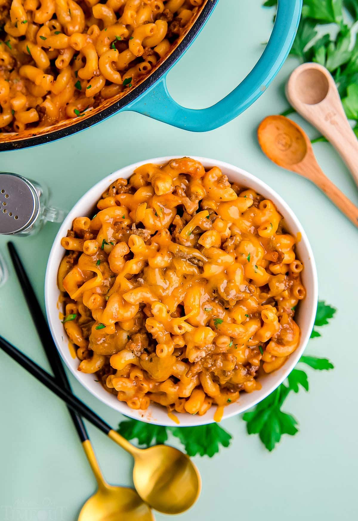 top down look at bowl of hamburger helper sitting next to skillet with the rest of it. light green background. 