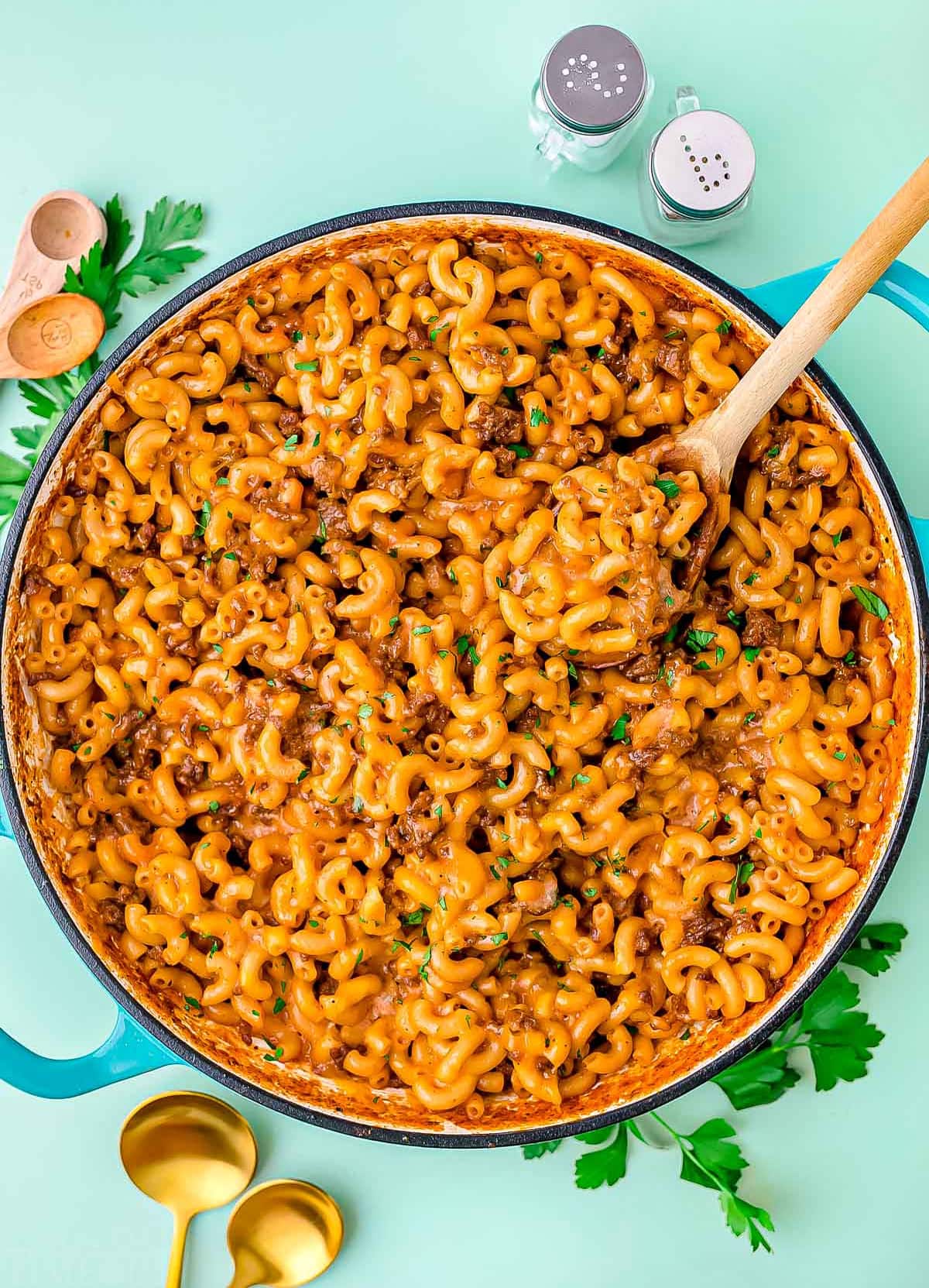 skillet of homemade hamburger helper garnished with chopped fresh parsley. background is light aqua colored.
