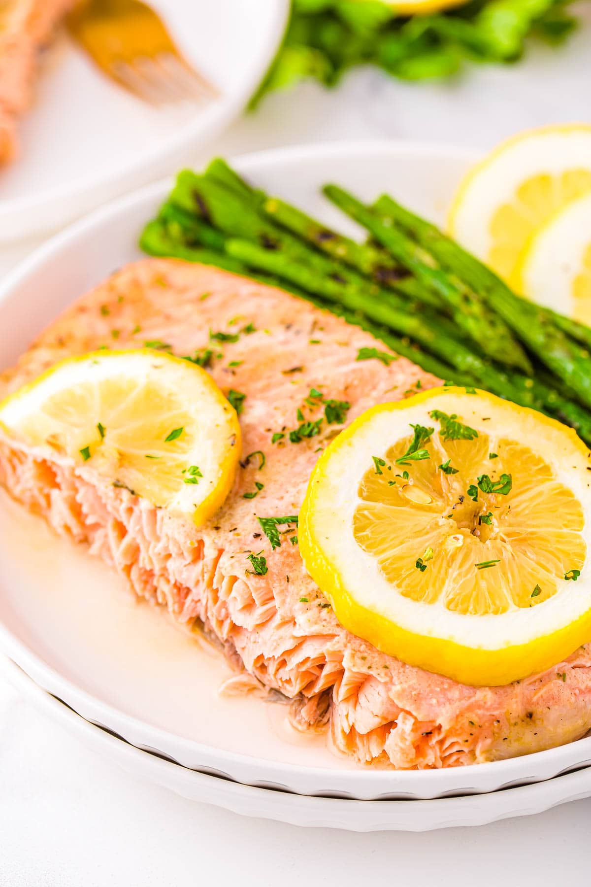 piece of baked salmon plated with asparagus and fresh lemon slices sitting on white plate.