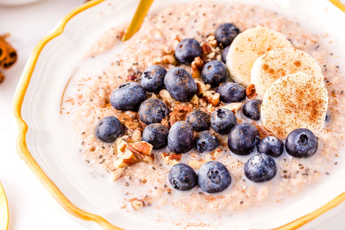 steel cut oatmeal topped with blueberries, pecans and cinnamon in a white bowl with a gold spoon.