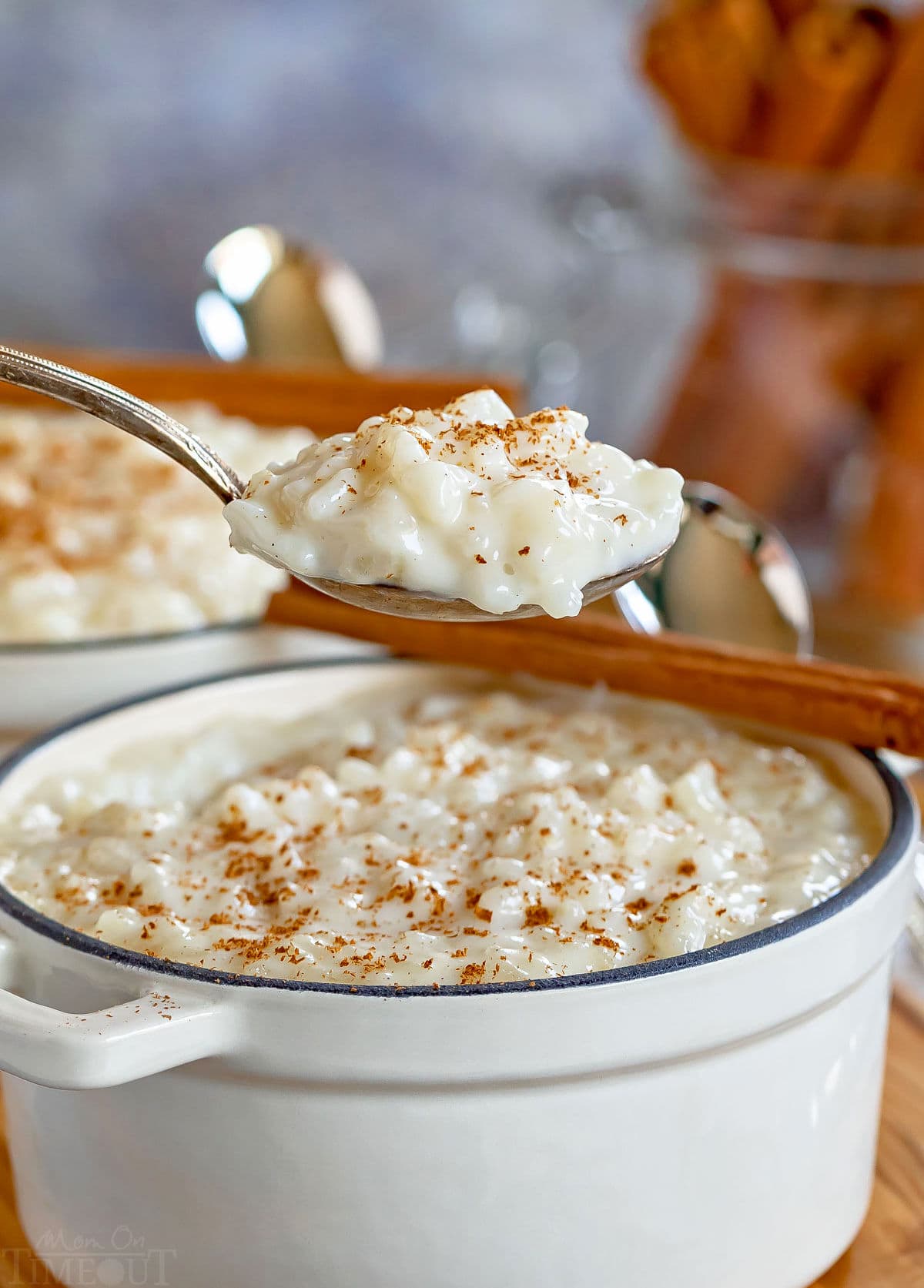 spoonful of rice pudding held up over the white pot it is being served from with freshly grated cinnamon stick on top. 