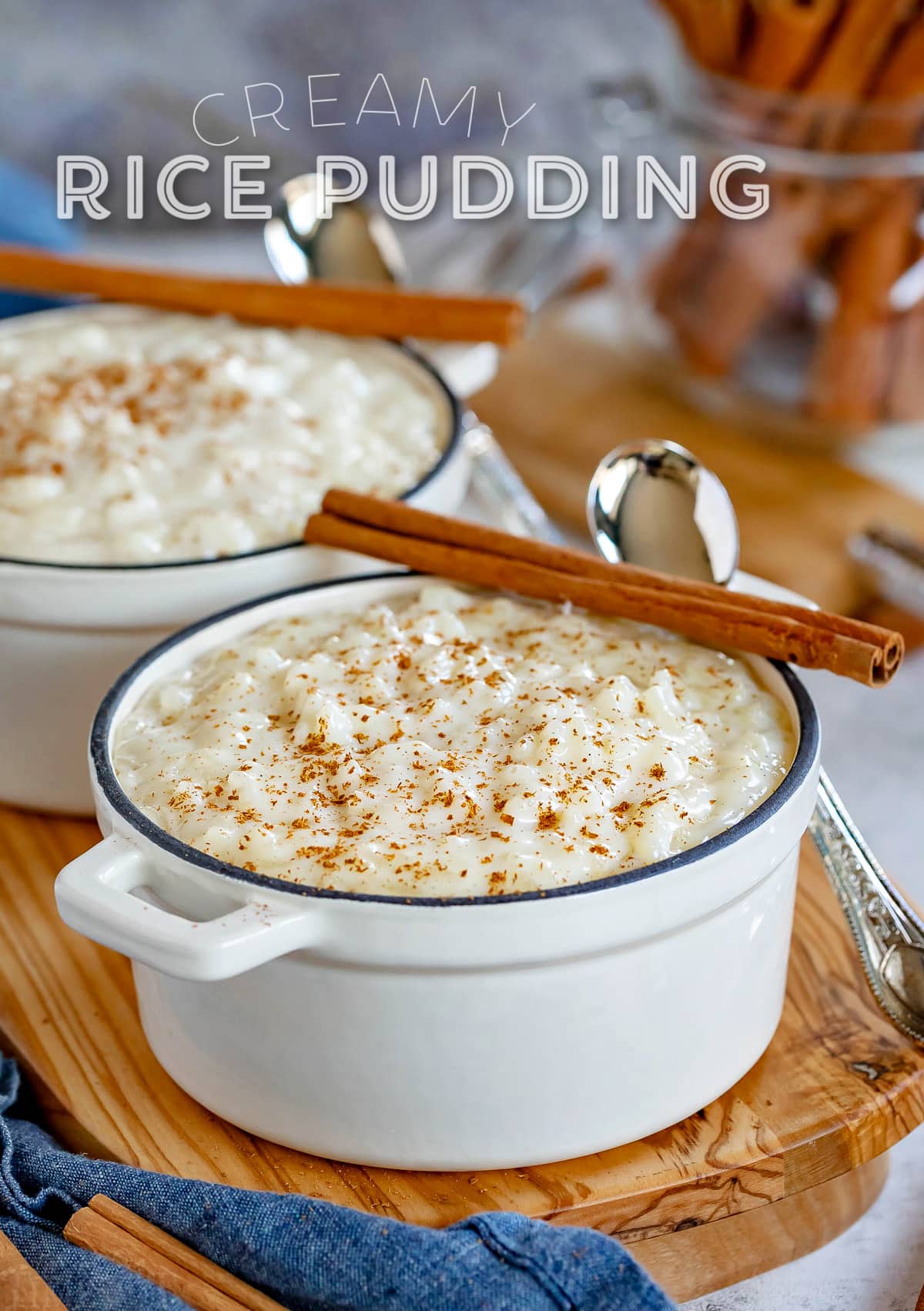 rice pudding served in 2 small white cast iron pots with cinnamon sticks resting on the rim. title overlay at top of image.