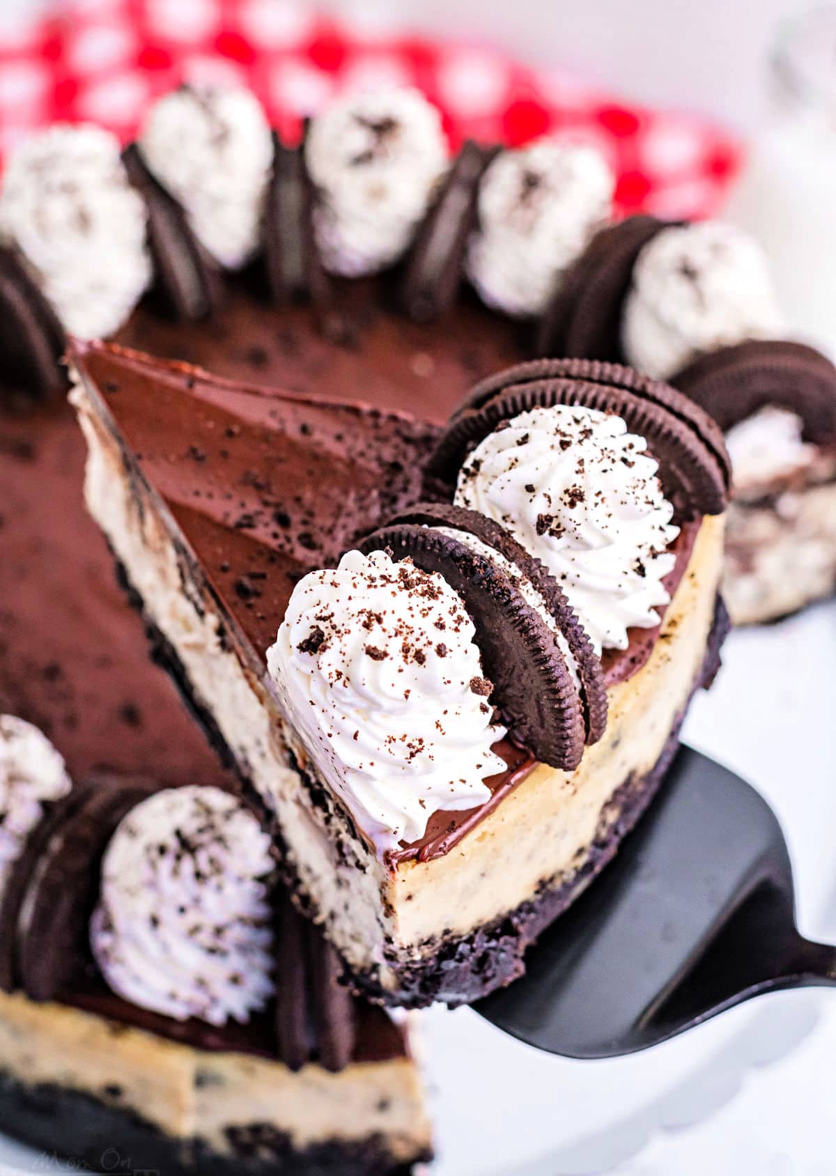 slice of oreo cheesecake being held above cake plate with rest of cheesecake.