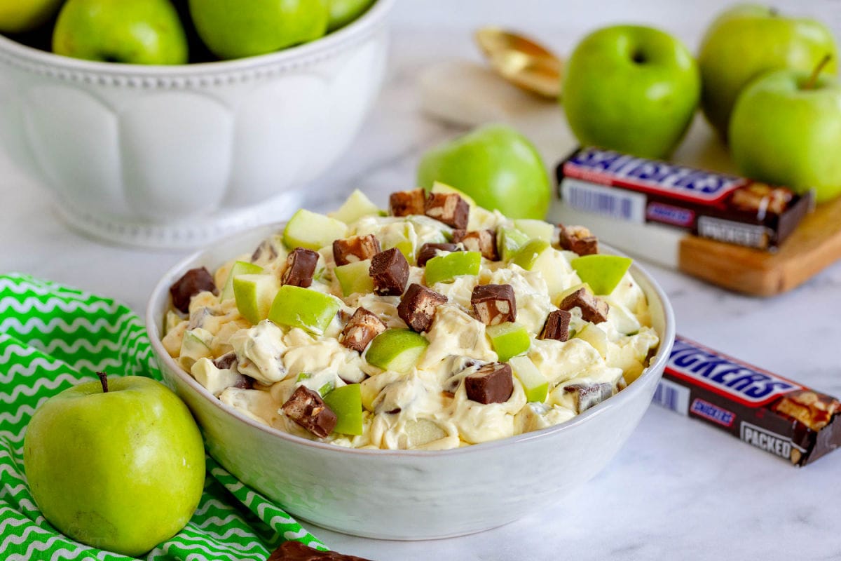 apple salad with snickers mixed in in large white bowl.