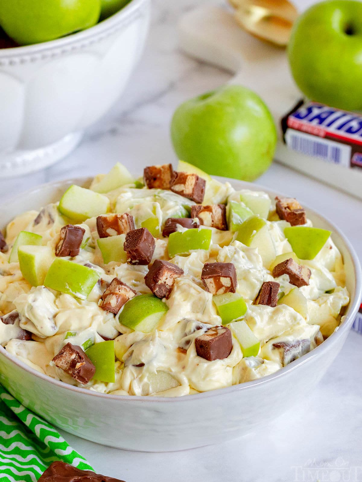 apple salad with snickers mixed in in large white bowl.