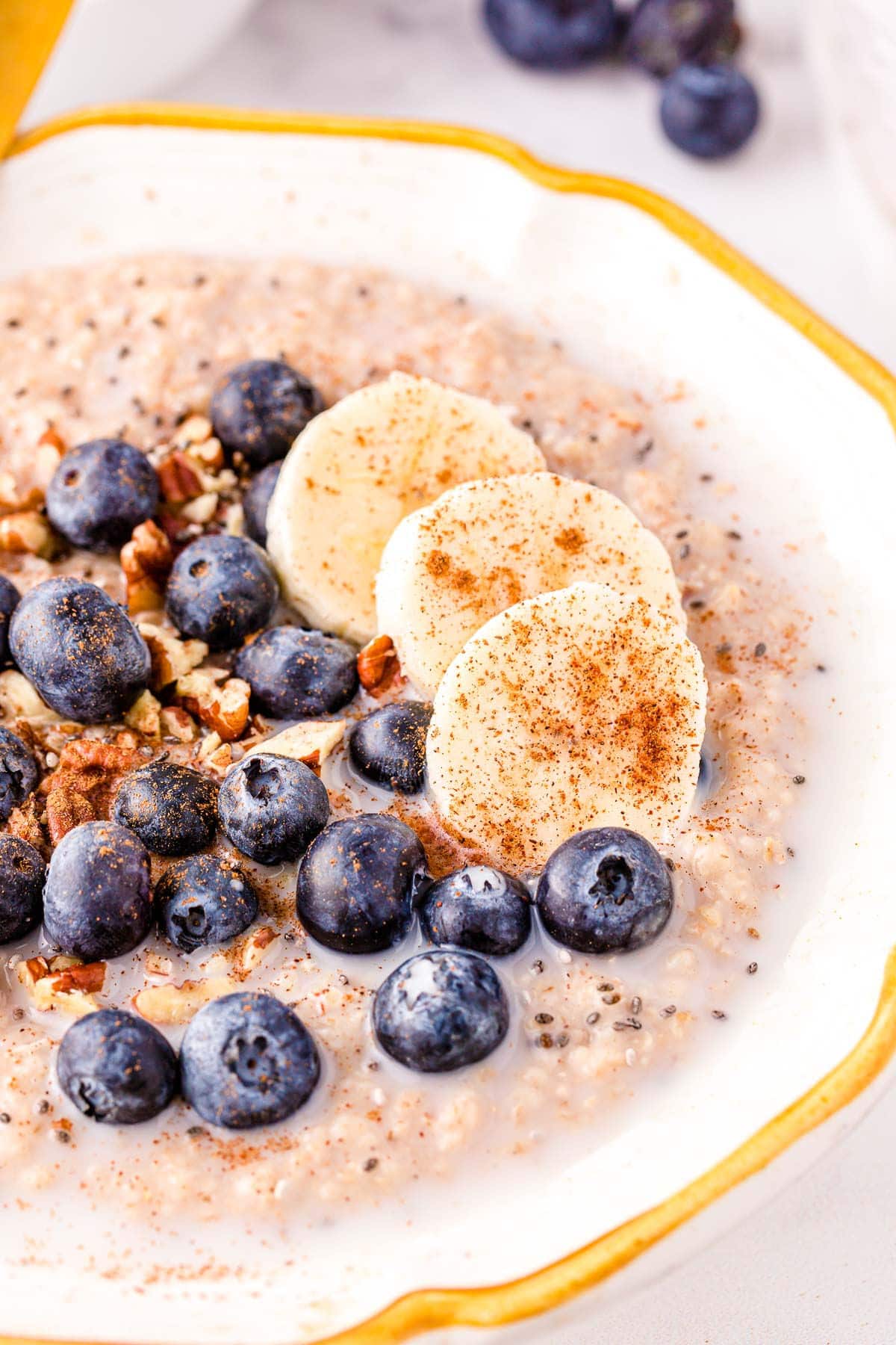 close up look at steel cut oats in bowl topped with blueberries, banana slices and pecans.