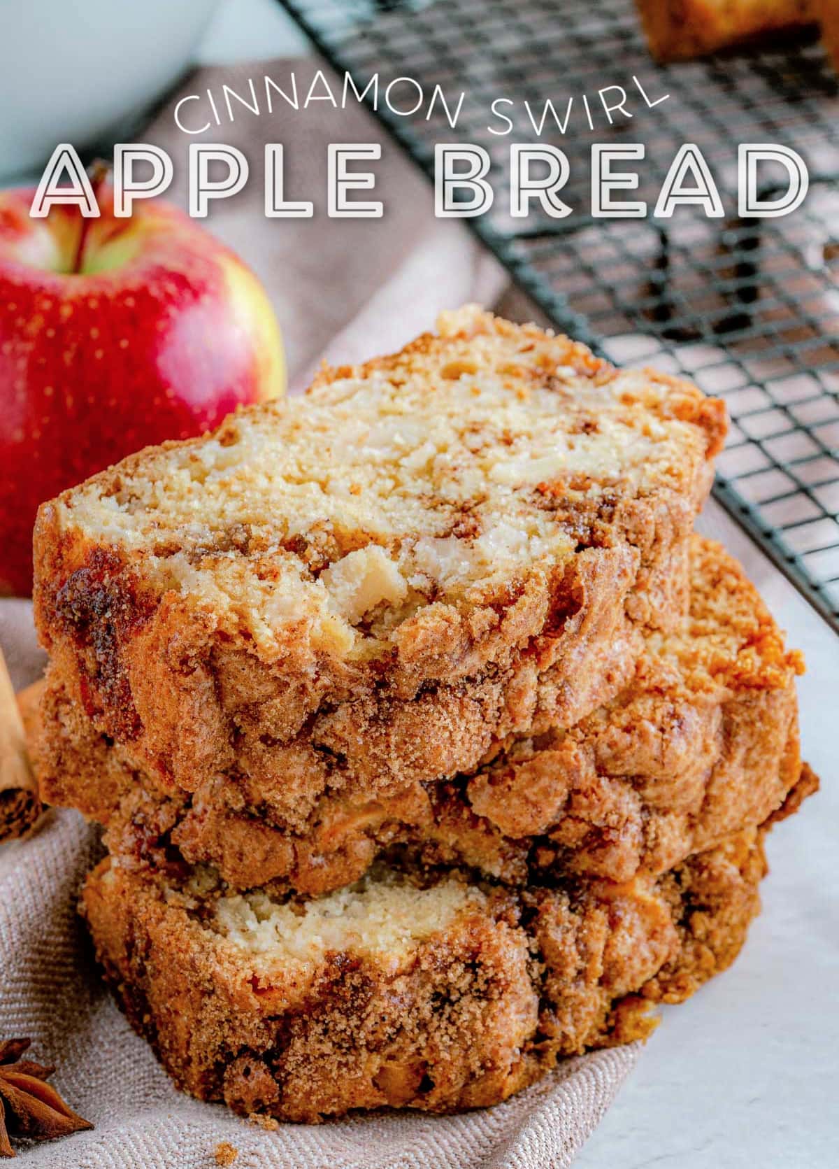 three slices of apple bread stacked next to a cooling rack with an whole red apple in background. title overlay at top of image.