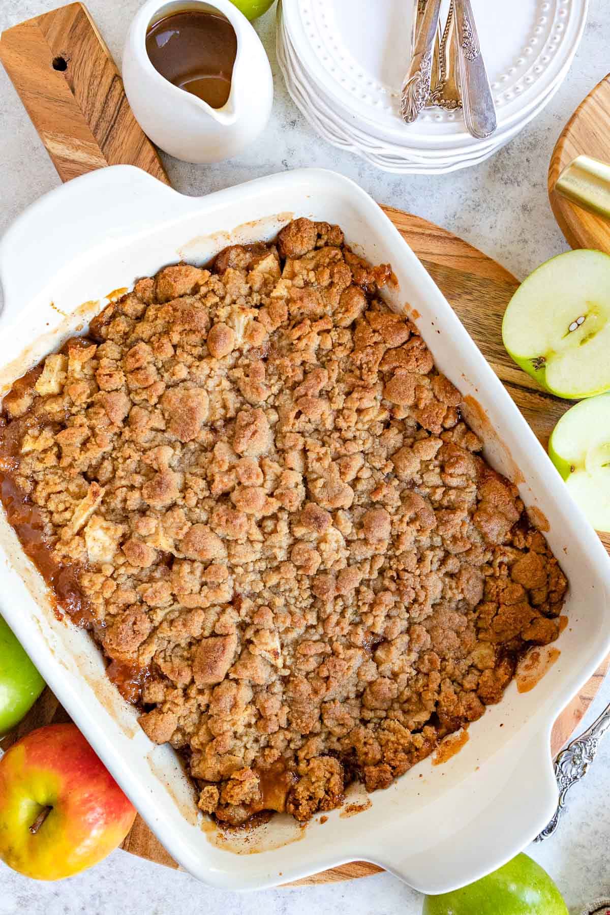 top down look at apple crumble in white baking dish sitting on wood cutting board.