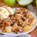 apple crumble served on a small white plate with vanilla ice cream and cut Granny Smith apples in background.