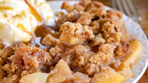 apple crumble served on a small white plate with vanilla ice cream and cut Granny Smith apples in background.