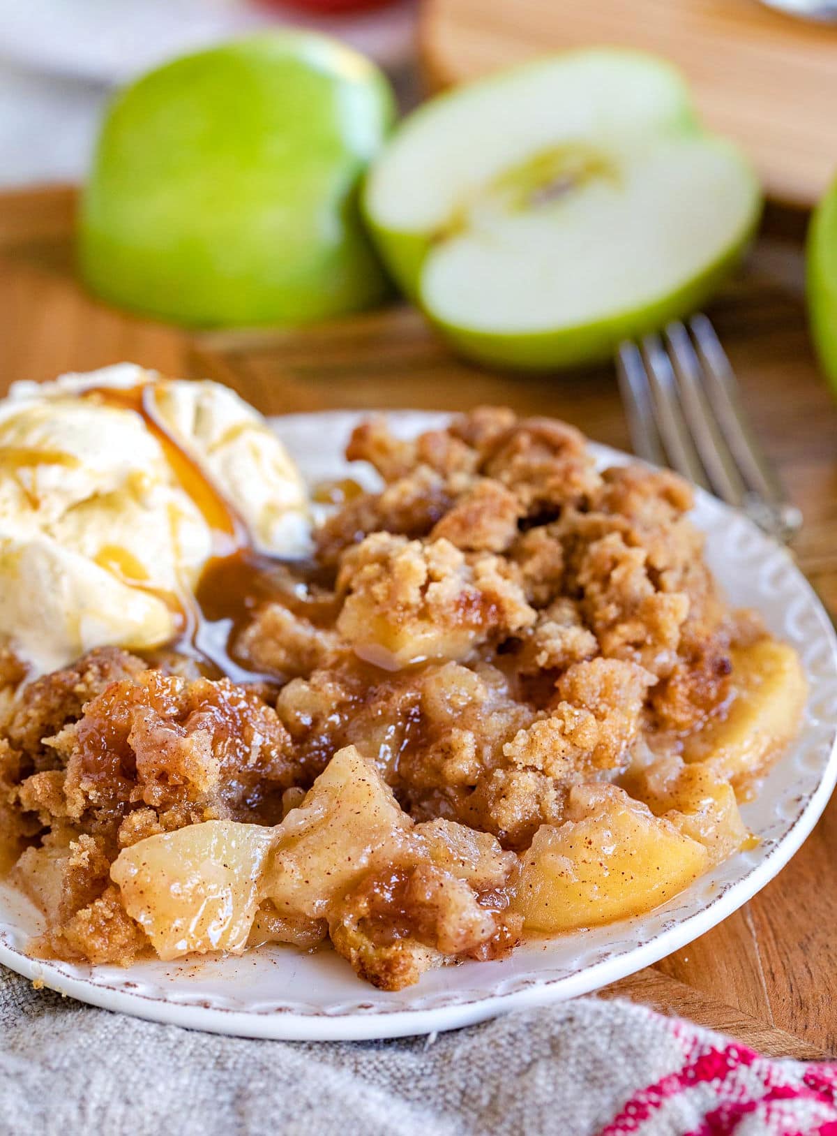 apple crumble served on a small white plate with vanilla ice cream and cut Granny Smith apples in background.