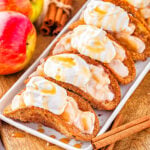 5 apple pie tacos on shallow white serving dish sitting next to blue and white striped napkin and fresh red apples.