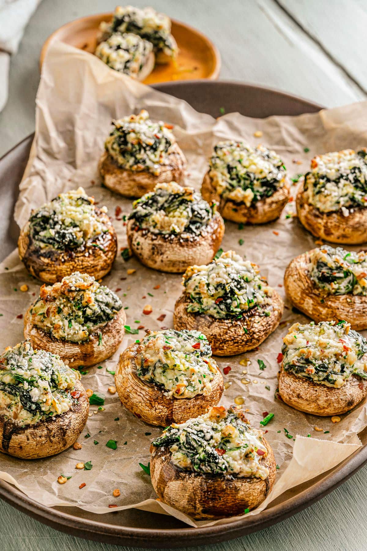 tray full of stuffed mushrooms sitting on crumpled brown parchment paper and sprinkled with fresh parsley.