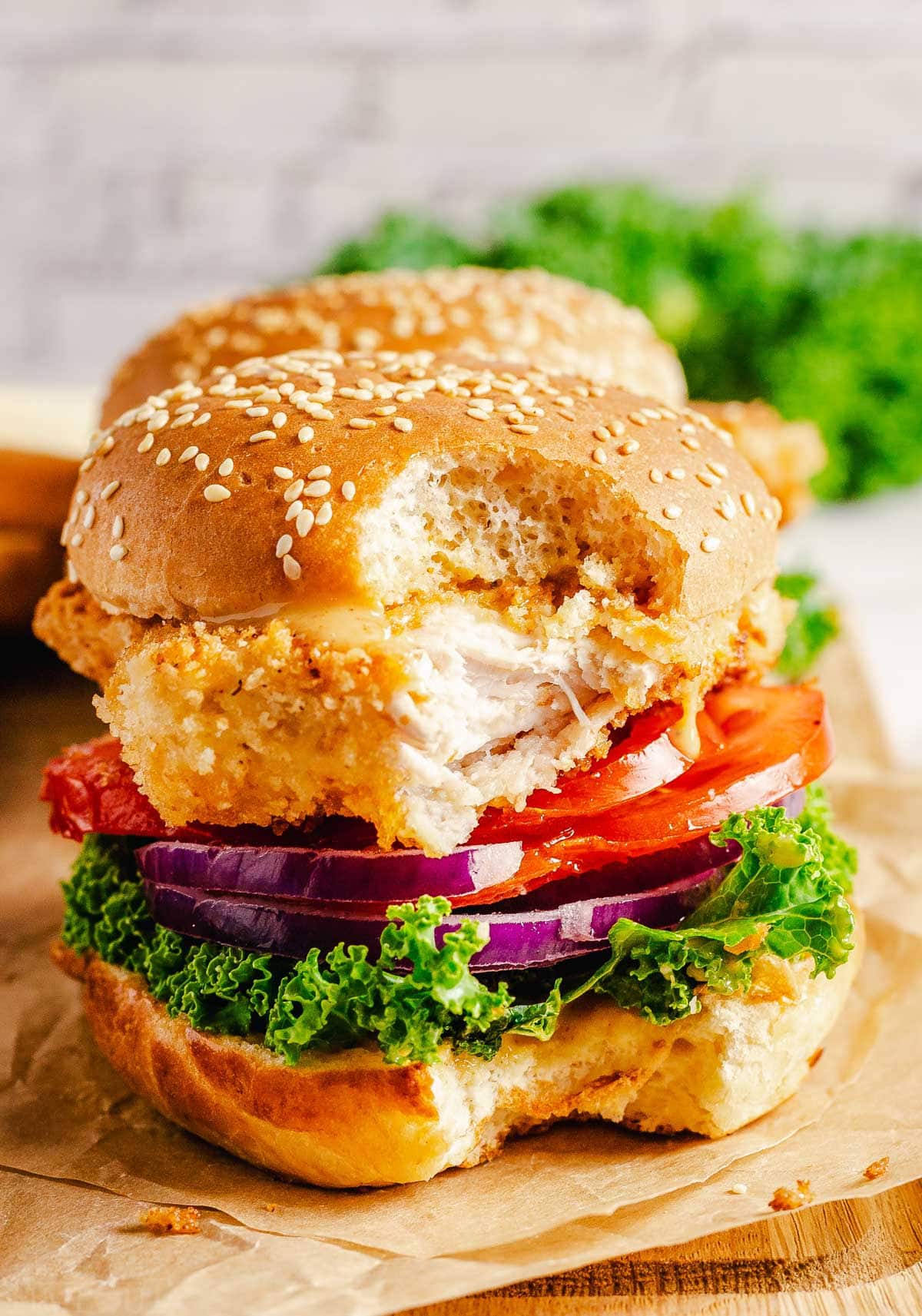 chicken sandwich with a big bite taken sitting on a brown parchment paper.