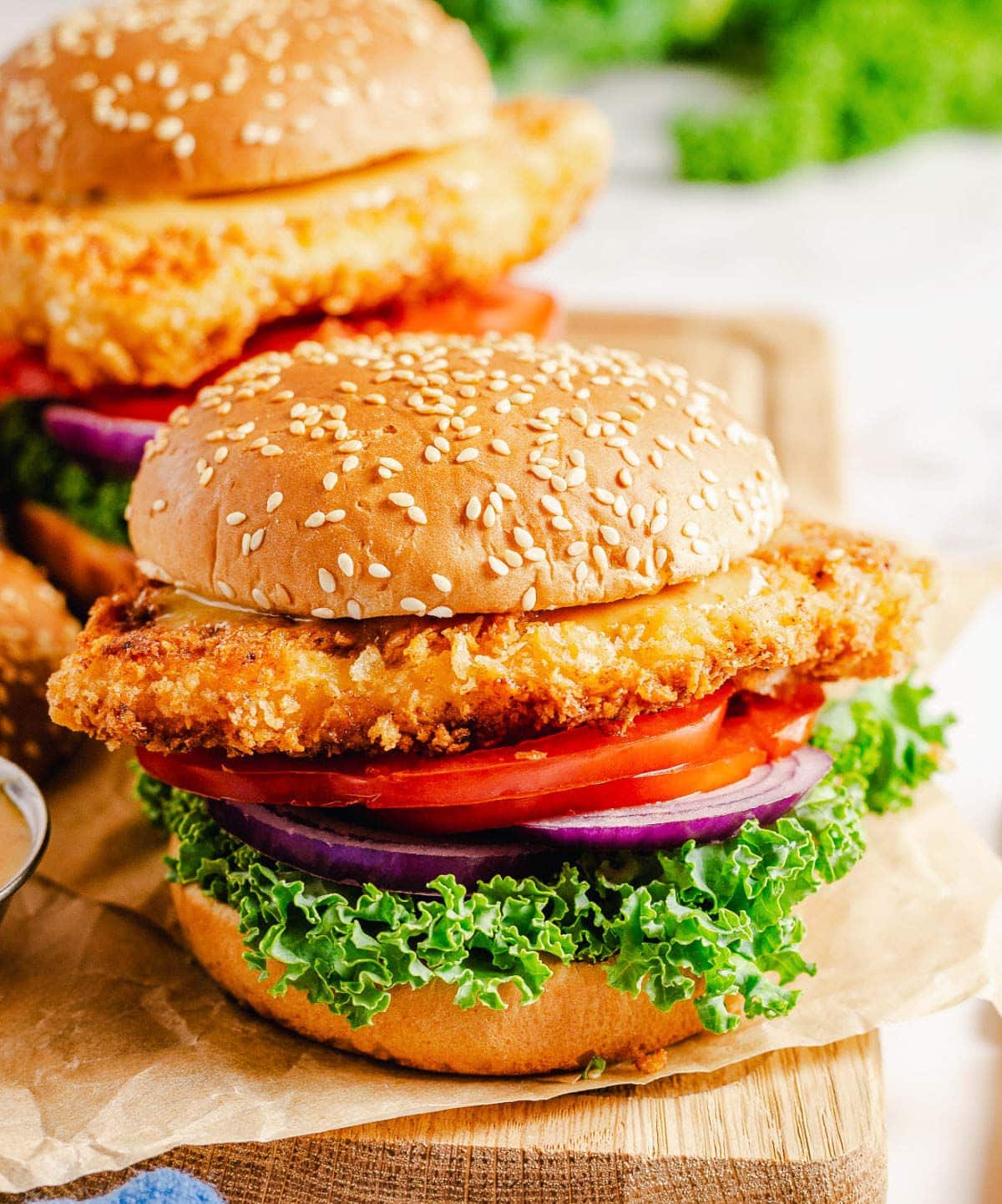 two chicken sandwiches on a wood board with all the fixins.