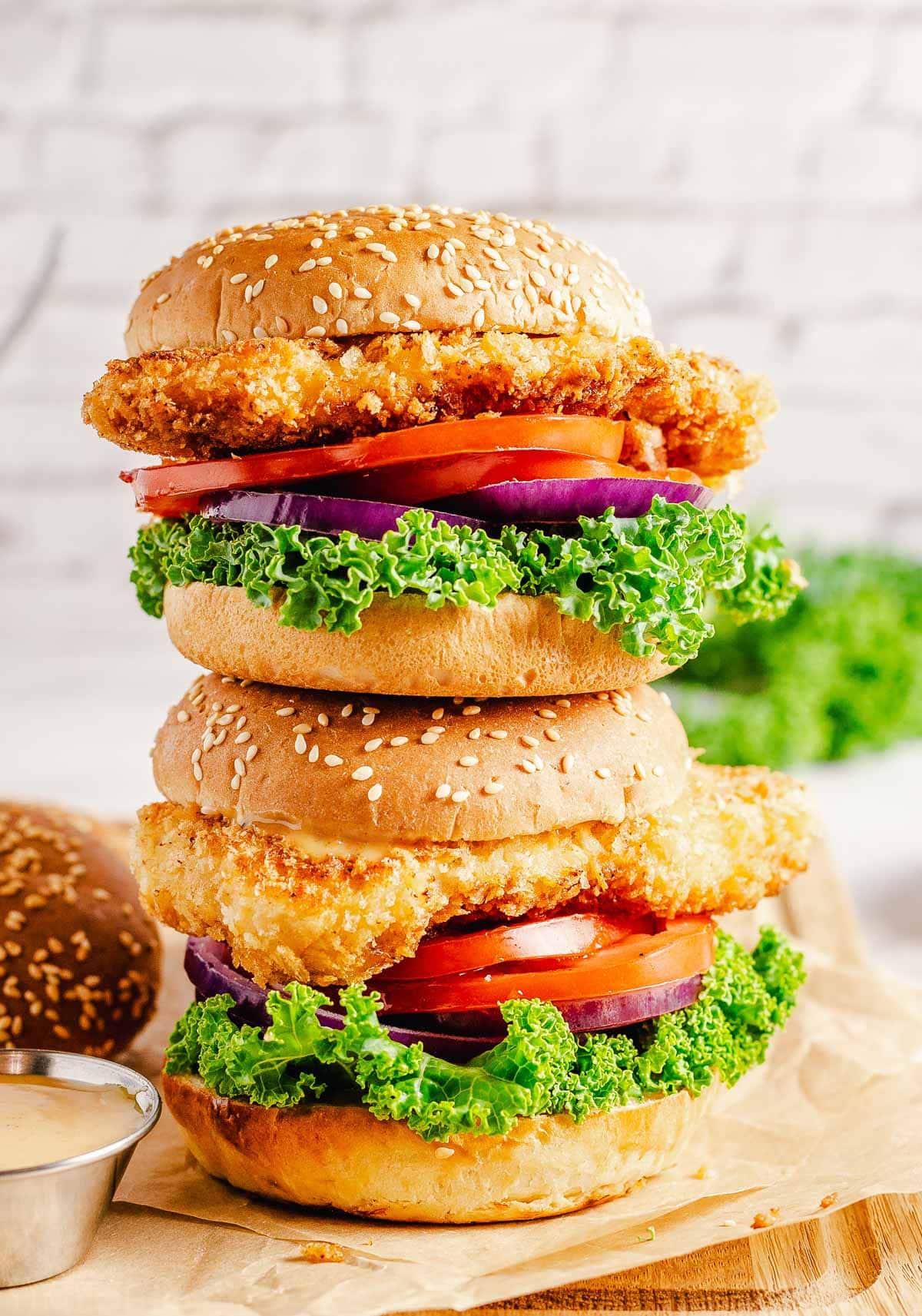 two chicken sandwiches stacked on each other sitting on wood cutting board.