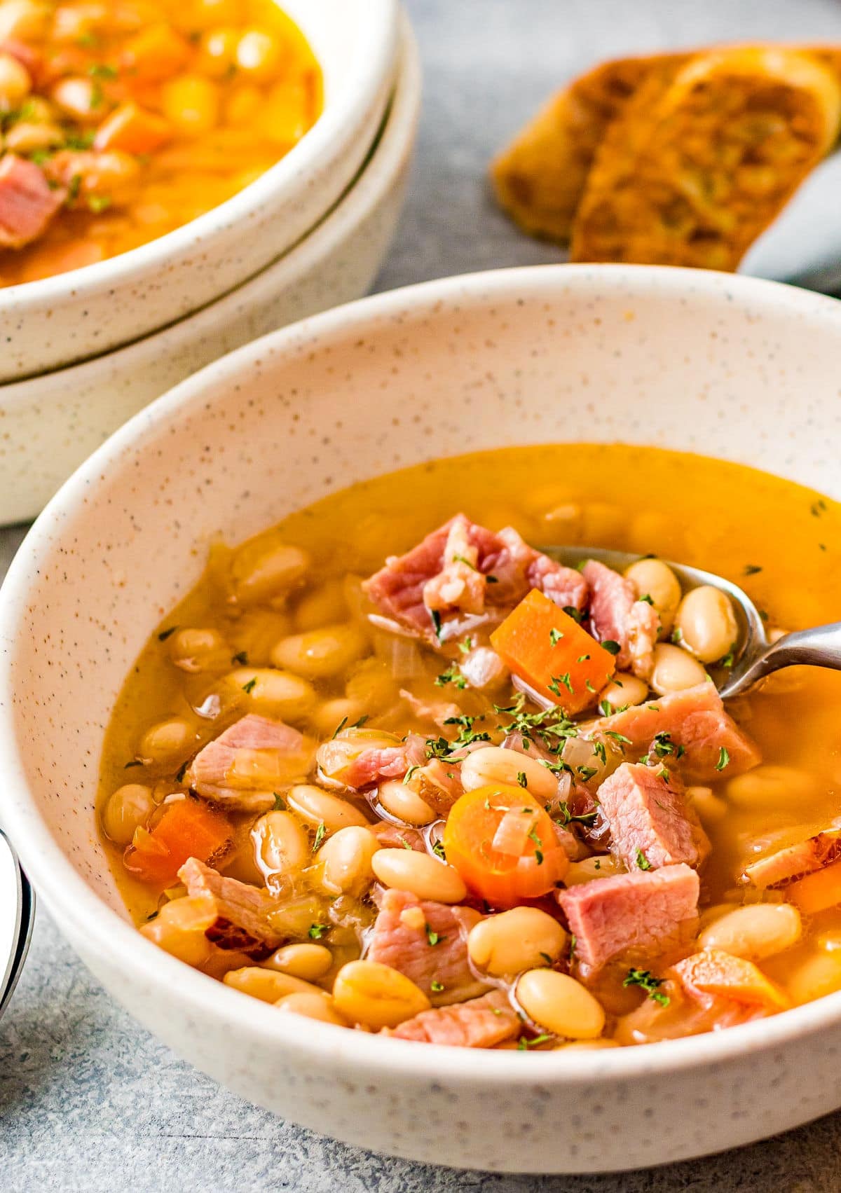 bowl full of ham and bean soup with lots of broth and a spoon.