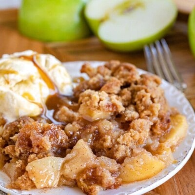 apple crumble served on a small white plate with vanilla ice cream and cut Granny Smith apples in background.