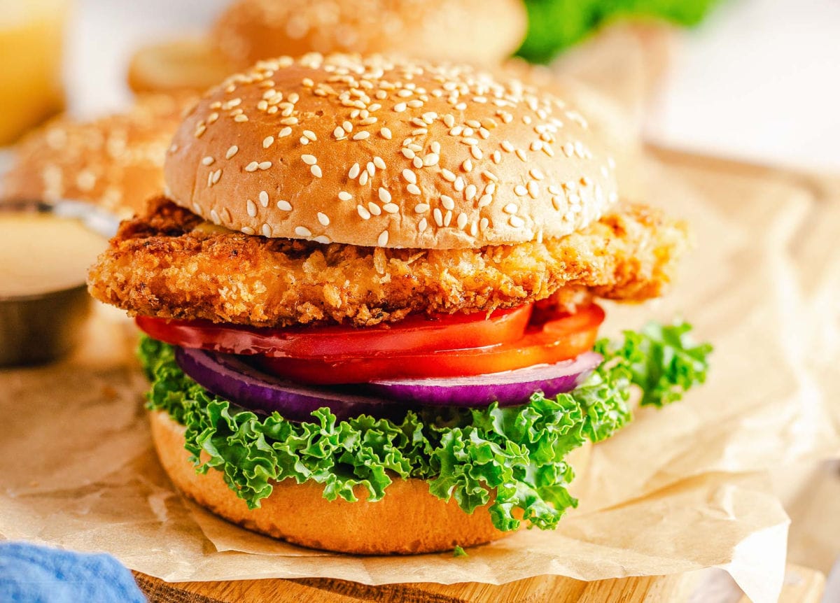 chicken sandwich with lettuce, red onion and tomato in a seeded bun.