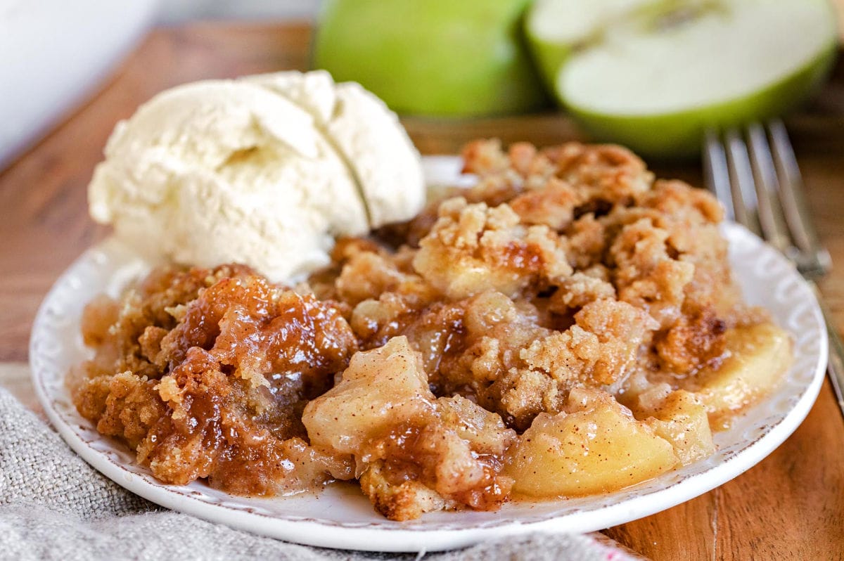 apple crumble served on a small white plate with vanilla ice cream and cut Granny Smith apples in background.