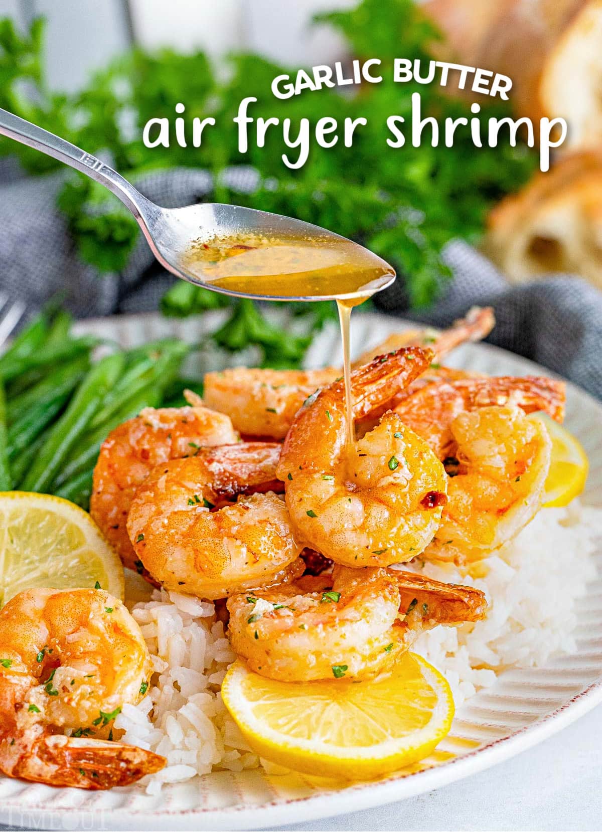 garlic her butter being drizzled on air fryer shrimp on a plate with green beans and lemon slices. title overlay at top of image.