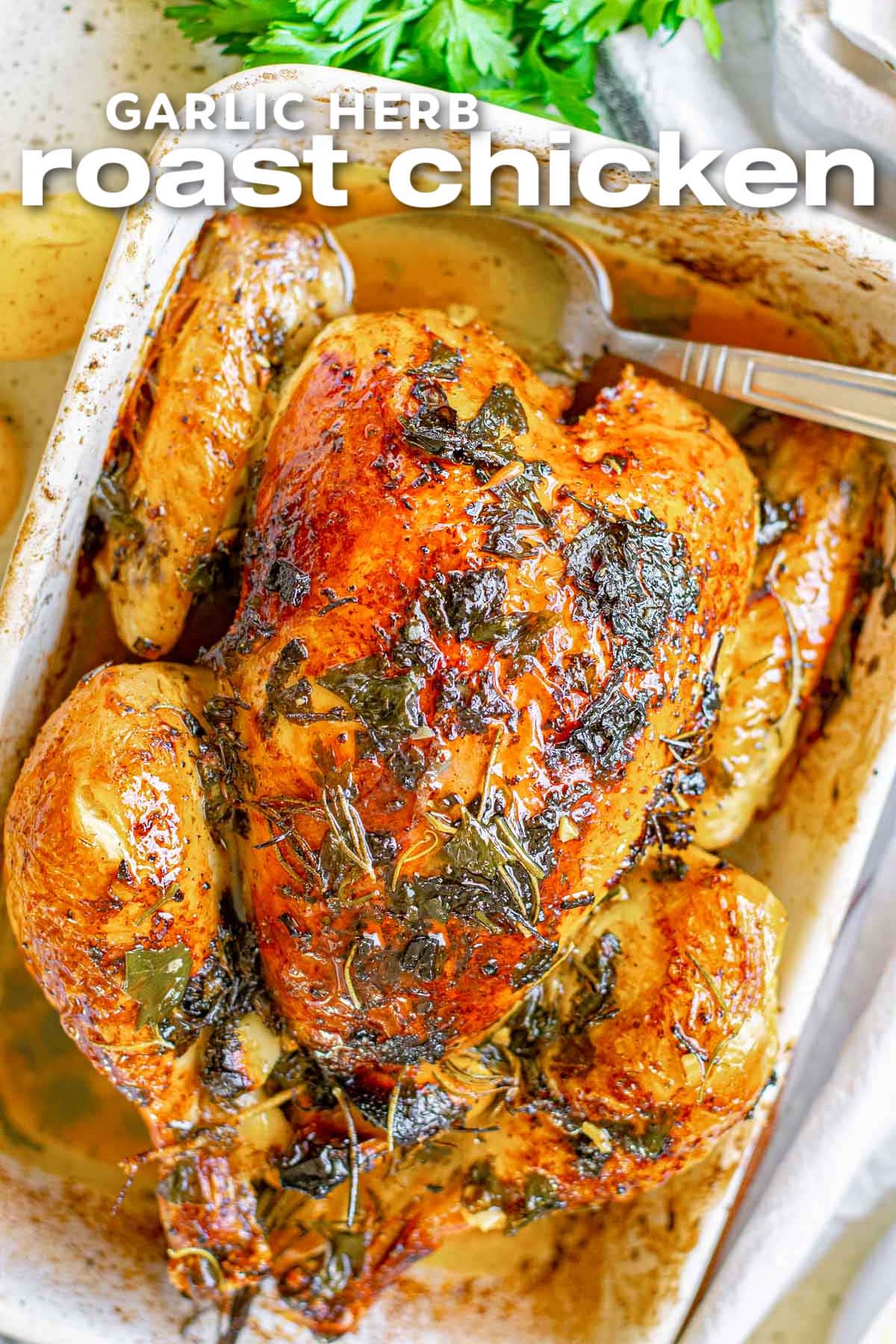 overhead look at roast chicken in white baking dish with crispy skin seasoned with fresh herbs. title at top of image.