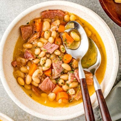 bowl of ham and bean soup with two spoons with wood handles next to pot of soup.