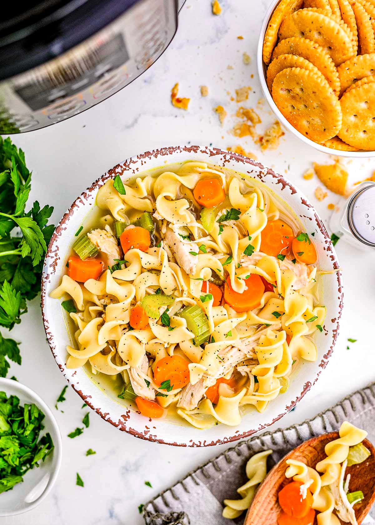 bowl of soup surrounded by a bowl of crackers, fresh parsley and sitting in front of a pressure cooker.