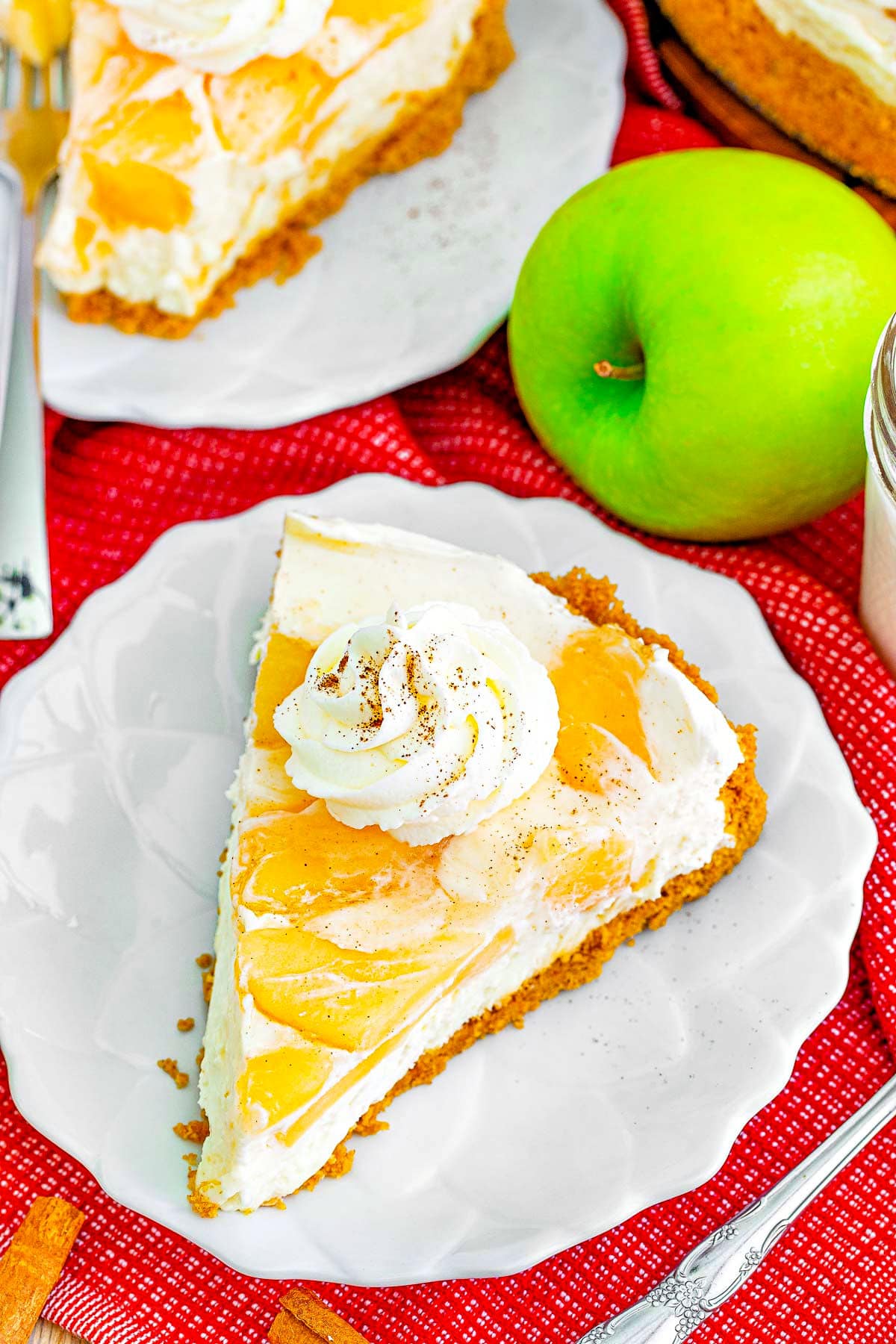 top down look at slice of apple cheesecake sitting on a small white dessert plate next to a granny smith apple.