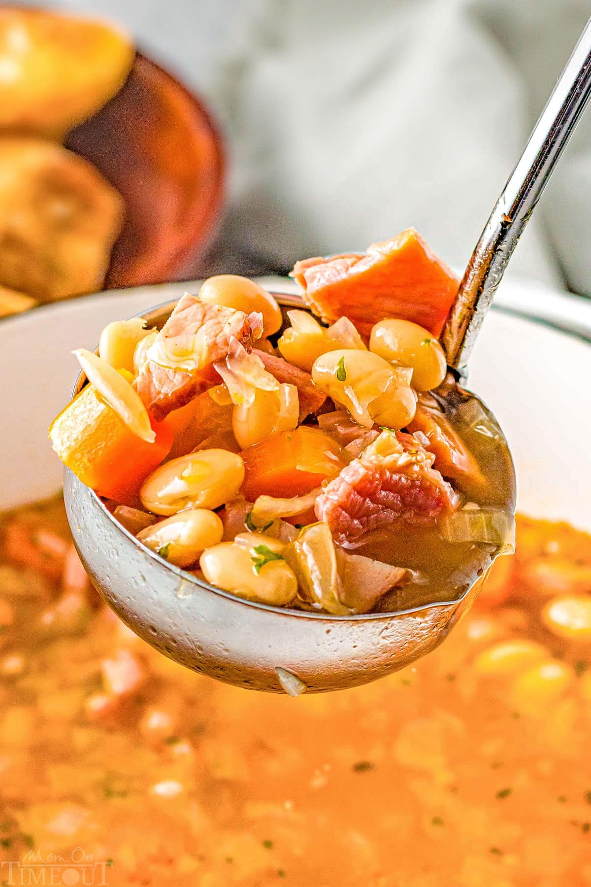 ladle full of ham and navy bean soup held above the pot of soup.