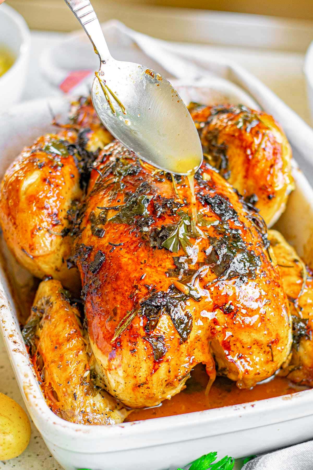 whole roasted chicken in baking dish with spoonful of pan juices being drizzled on top of the whole chicken.
