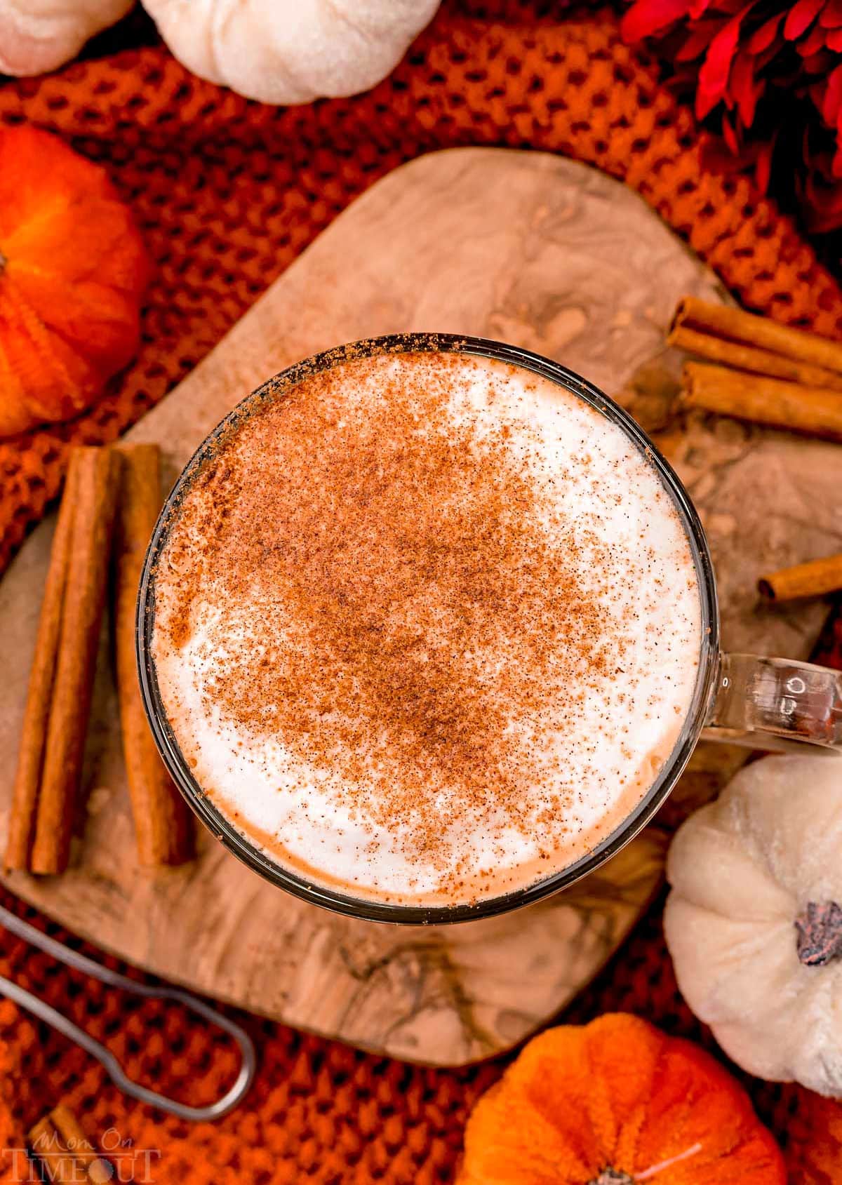 top down look at psl on olive board with cinnamon sticks resting near the glass mug.