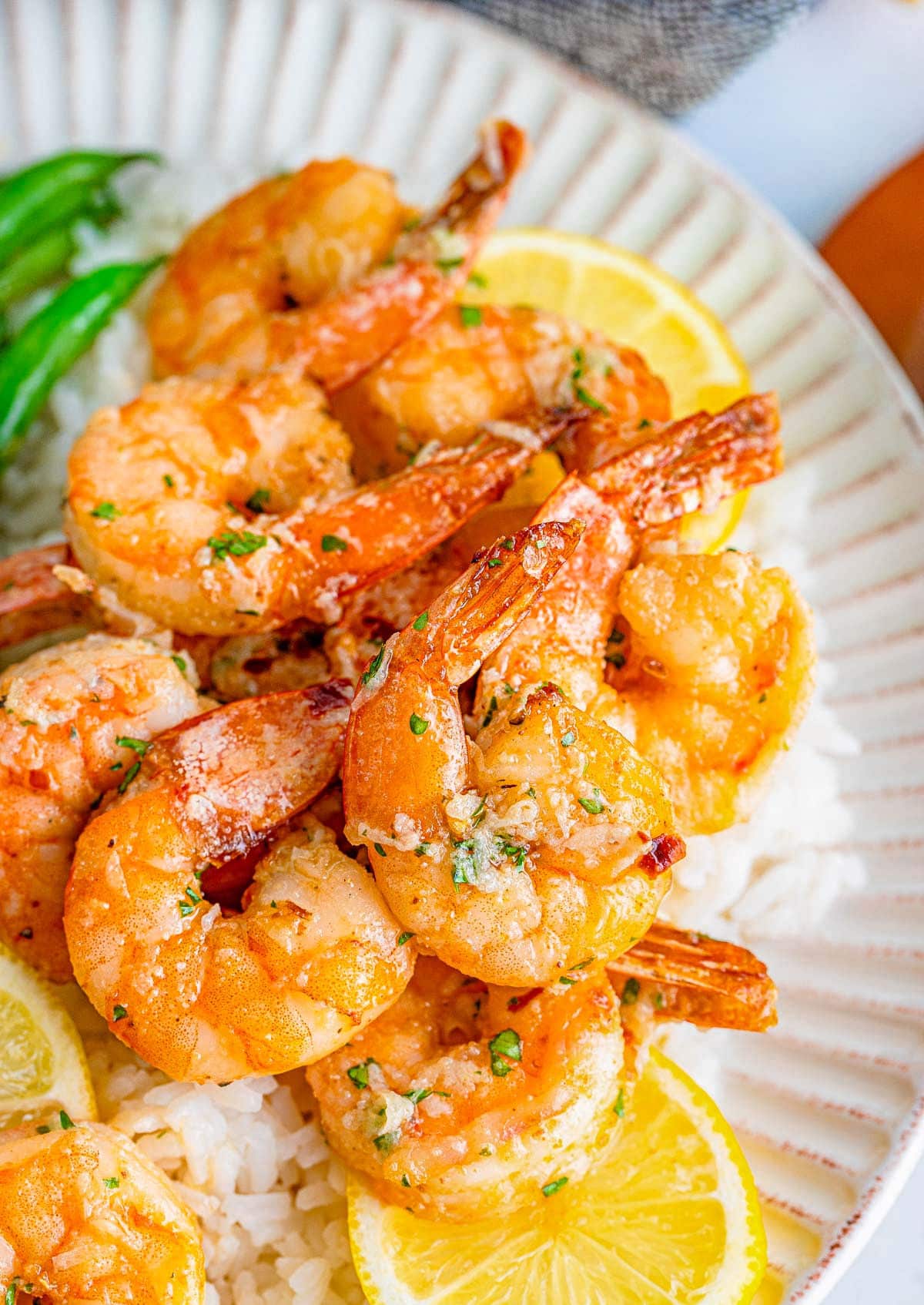 top down close up look at air fryer fried shrimp on a plate with lemon slices all topped with a garlic butter sauce.