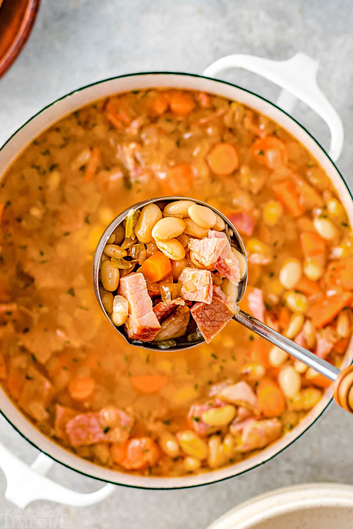 top down look at ladle being held above pot of soup in white dutch oven.