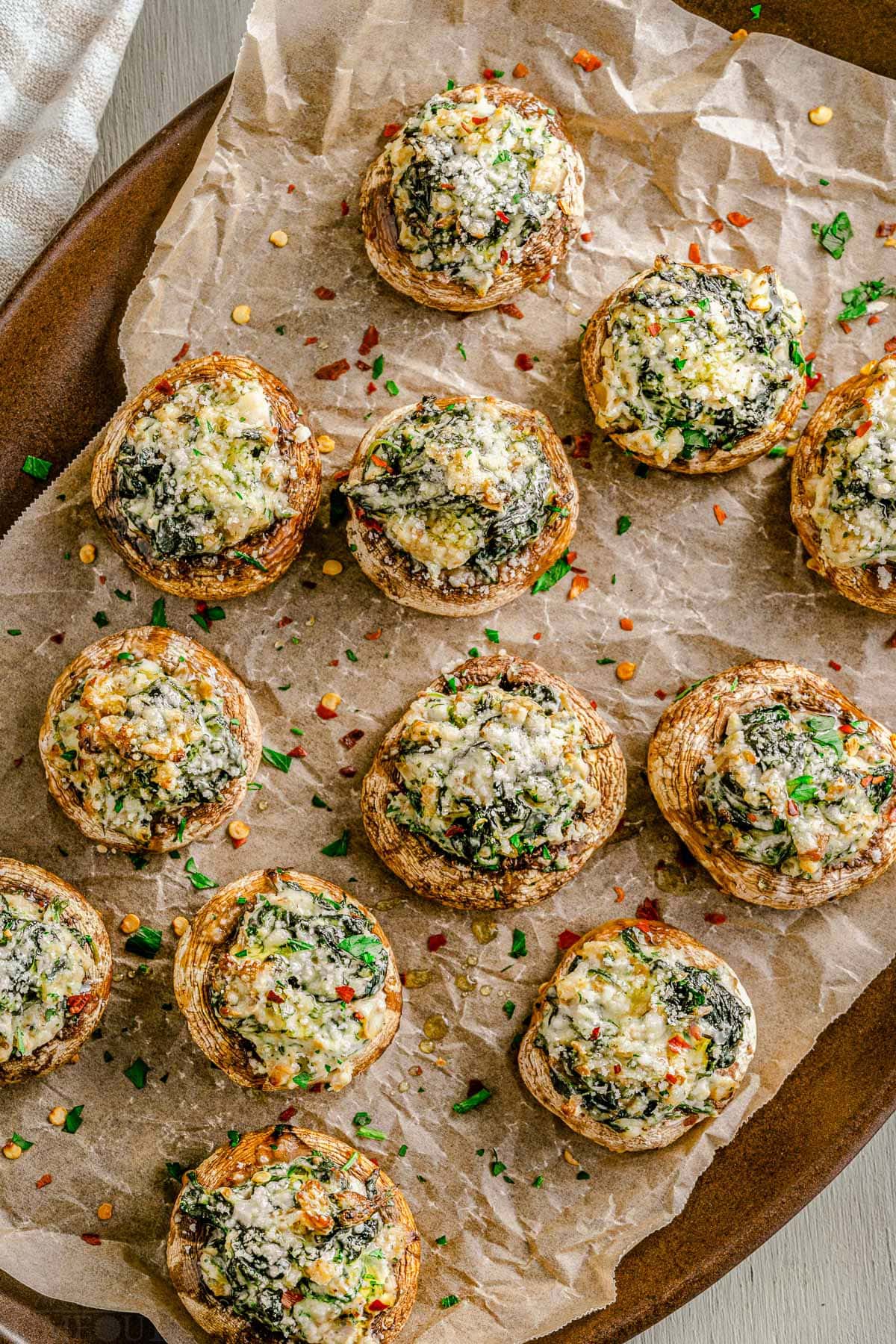 tray full of stuffed mushrooms sitting on crumpled brown parchment paper and sprinkled with fresh parsley.