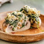 a stuffed mushroom split in half on a brown plate so you can see the creamy spinach filling.