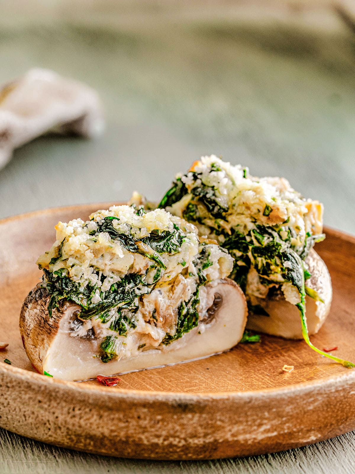 a stuffed mushroom split in half on a brown plate so you can see the creamy spinach filling.