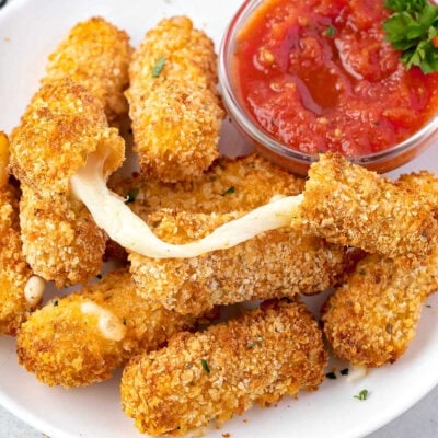 cheese stick with a cheese pull sitting on top of more mozzarella sticks on white plate.