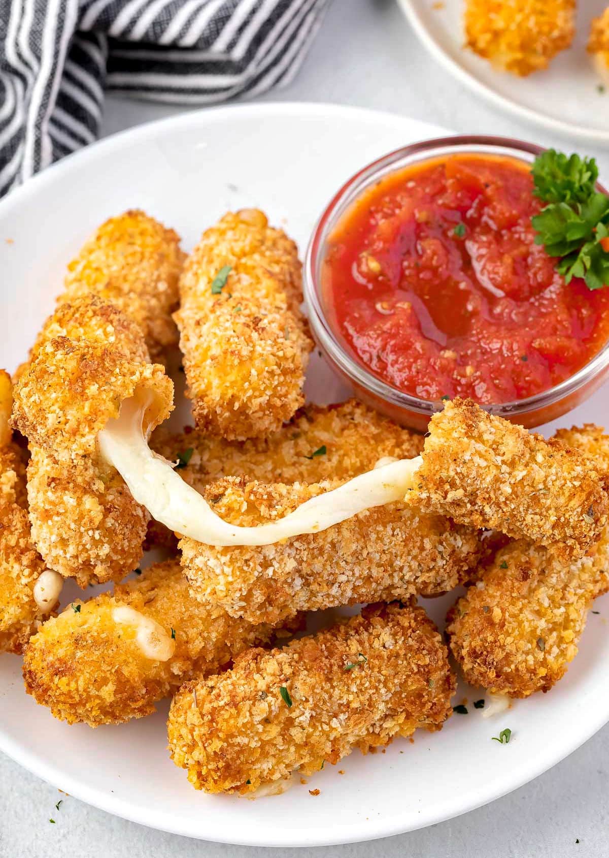 cheese stick with a cheese pull sitting on top of more mozzarella sticks on white plate.