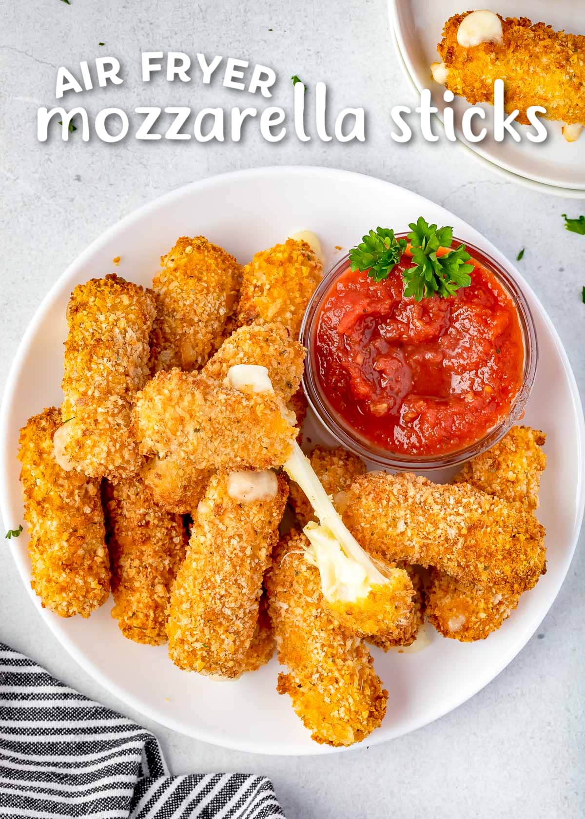 pile of air fryer mozzarella sticks on a white plate with marinara sauce. title overlay at top of image.