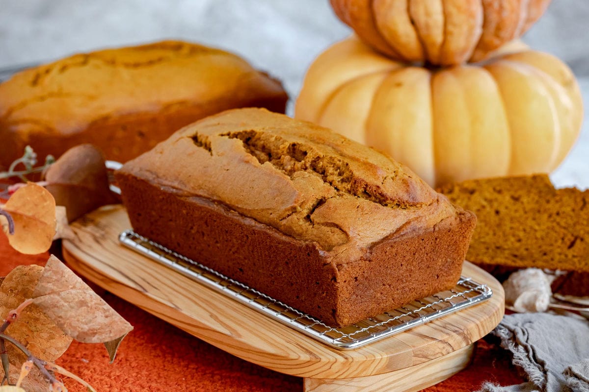 whole loaf of pumpkin bread on olive board with another loaf in background.