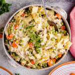 chicken and noodles recipe served in a stoneware bowl and topped with a sprig of thyme.