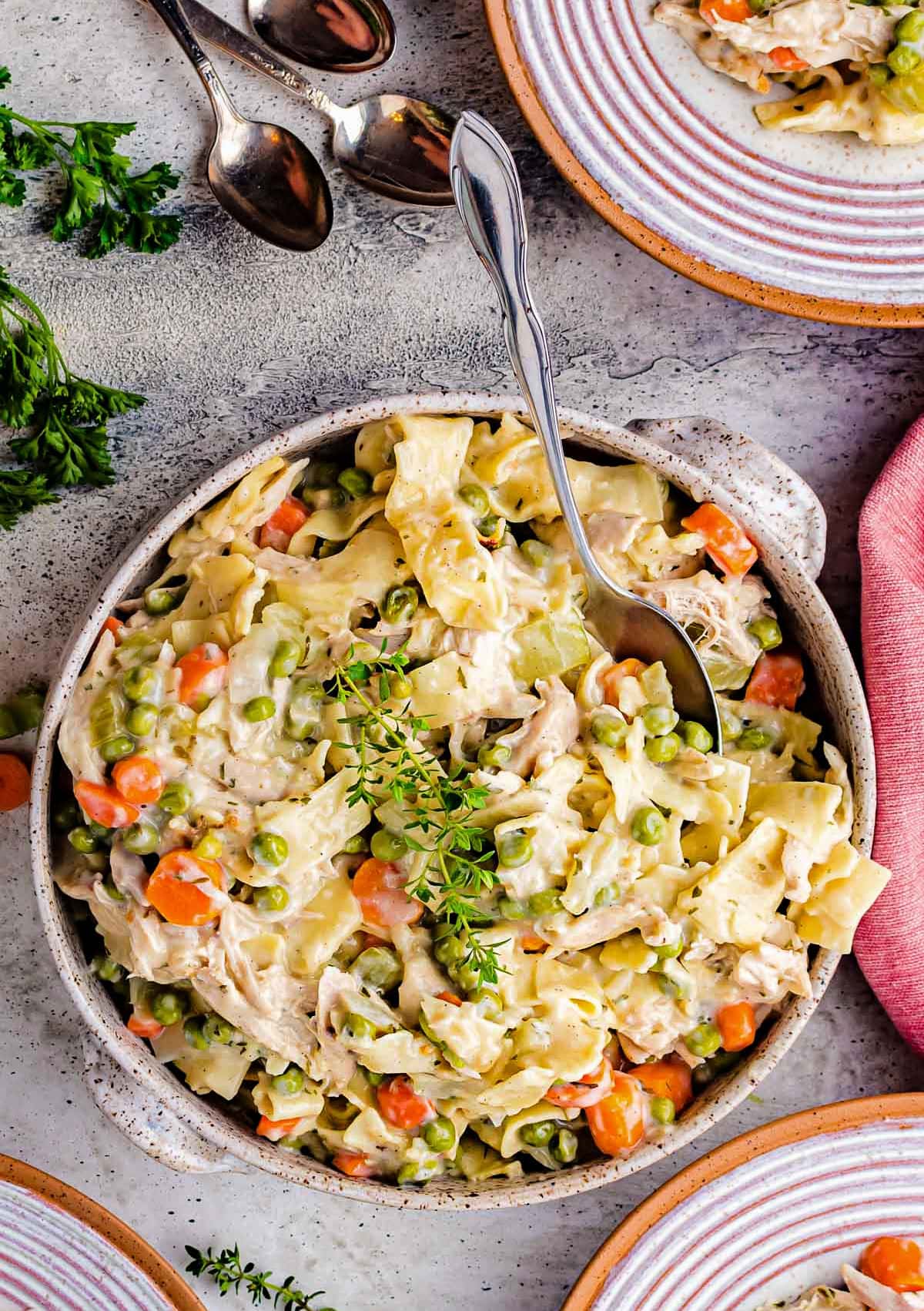 chicken and noodles recipe served in a stoneware bowl and topped with a sprig of thyme.