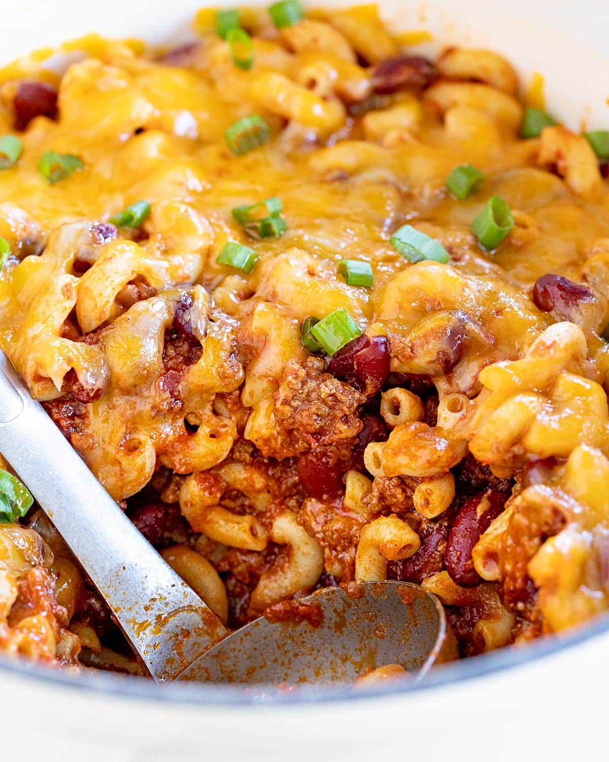 scoop of chili mac removed from large white dutch oven.