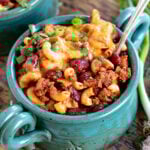 teal bowl filled with chili mac and topped with shredded cheese and sliced green onions.