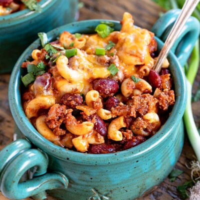 teal bowl filled with chili mac and topped with shredded cheese and sliced green onions.